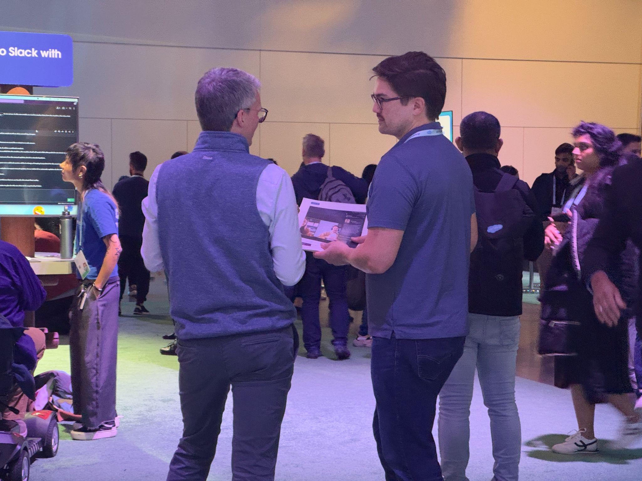 Two attendees at the Slack booth at Dreamforce reviewing a printed concept